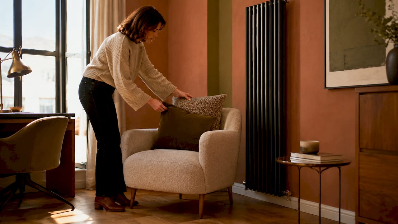 Woman arranging cushions near modern radiator in living room