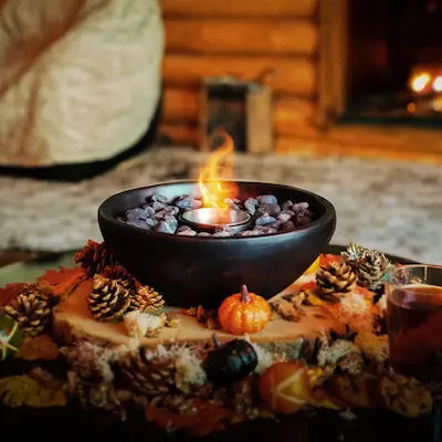 Round black bio ethanol tabletop fireplace with flame, placed on an autumn-themed table with pinecones and mini pumpkins
