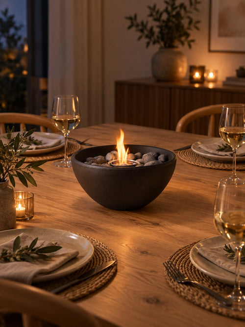 Black round bio-ethanol tabletop fireplace lit on a set dining table in the evening